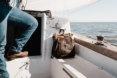 穿着蓝色牛仔牛仔裤的人坐在游艇旁边的棕色包里